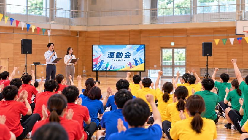 100インチ大型モニターでオープニング映像が流れる小規模体育館での運動会の様子